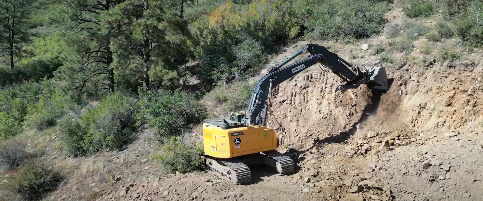 A John Deere excavator digging into a mountainside to make a road.